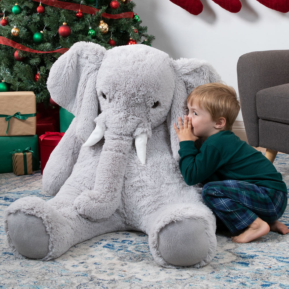 Child playing with a large plush elephant toy in front of a Christmas tree.