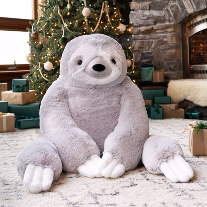Giant sloth stuffed animal in a festive room with a Christmas tree and presents.