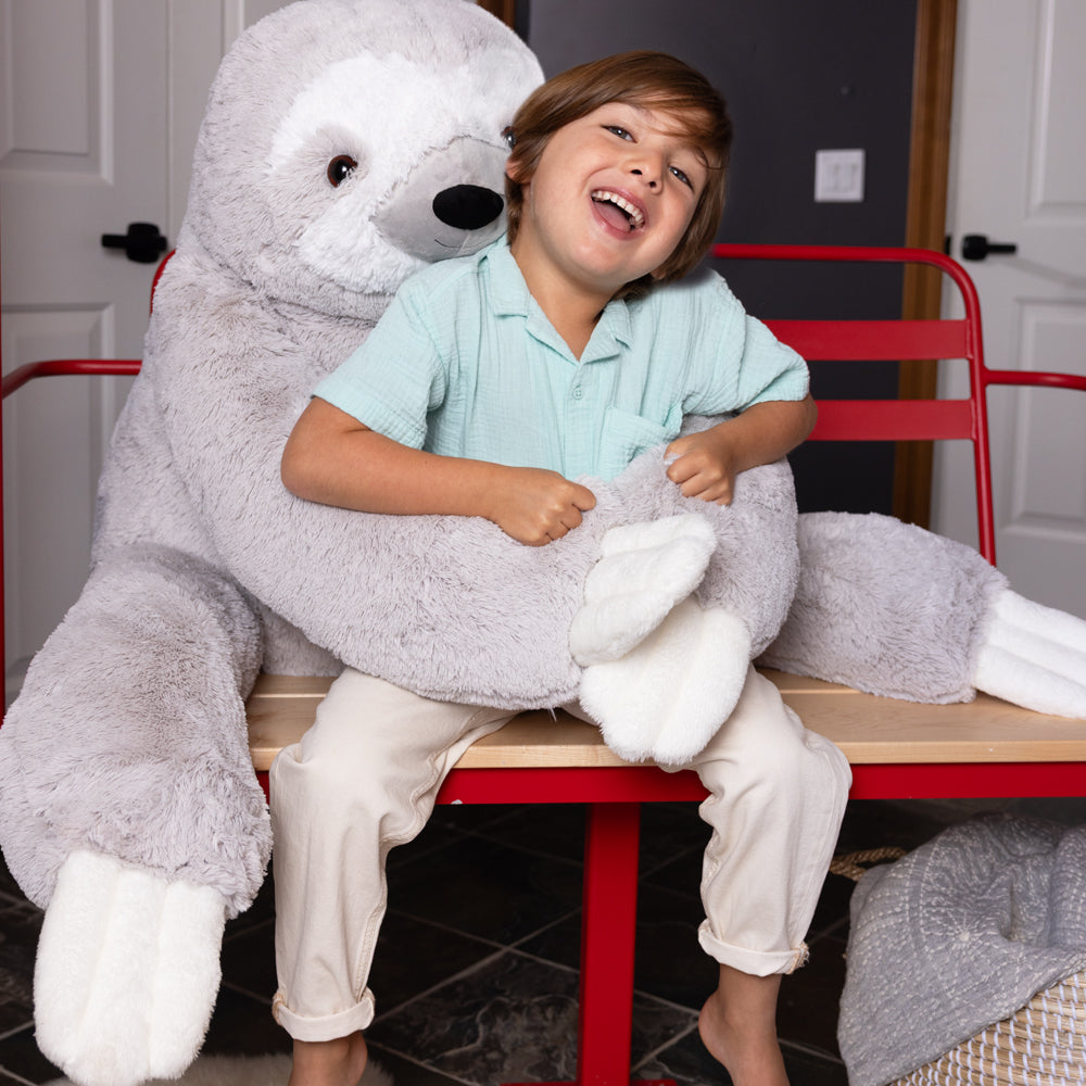 Child sitting on a red chair with a large gray plush sloth animal