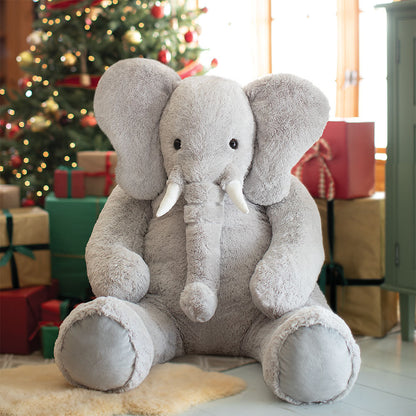Large plush elephant toy in front of a decorated Christmas tree with presents.