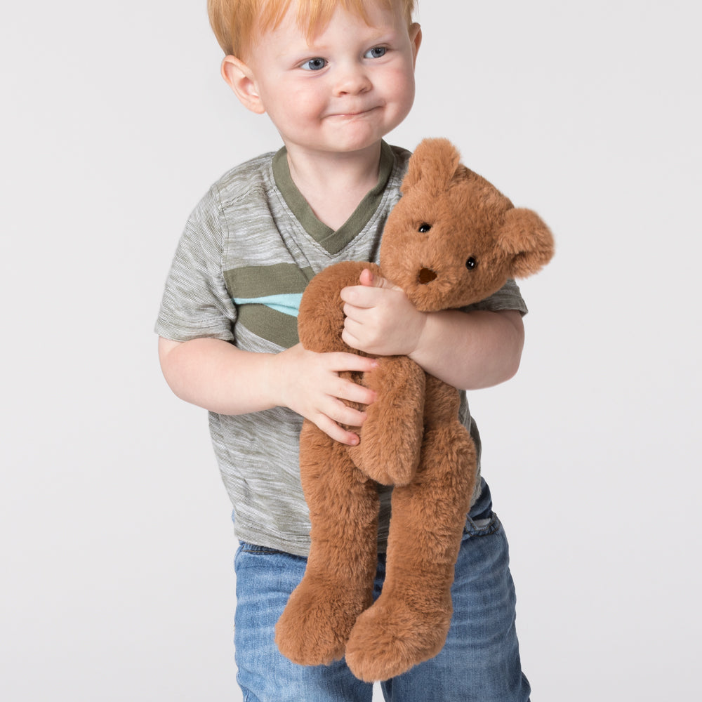 Toddler boy in striped shirt holding a soft brown teddy bear with long legs.