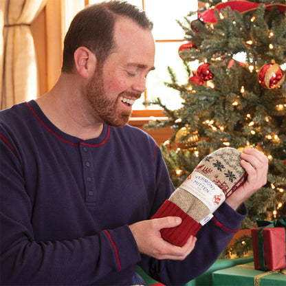 Man holding a pair of mittens with a Christmas tree in the background
