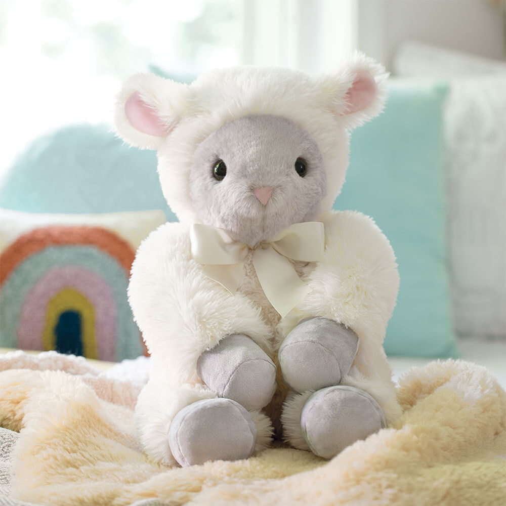 Plush lamb toy with white fleece, gray face and paws, and a cream bow sitting on a soft beige blanket.