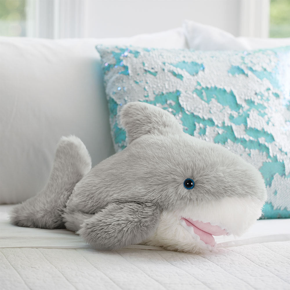 Gray plush shark toy with soft fur, black eyes, pink mouth, and white underbelly on a white couch.