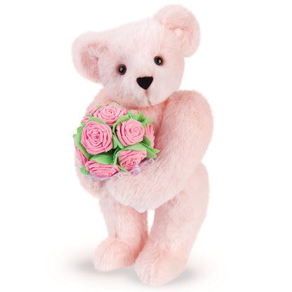 Soft pink teddy bear holding a bouquet of bubblegum pink rose-shaped roses with green leaves.