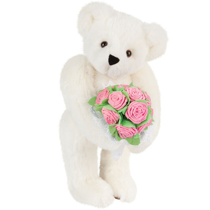 White plush teddy bear holding a bouquet of pink rose foam flowers with green leaves.