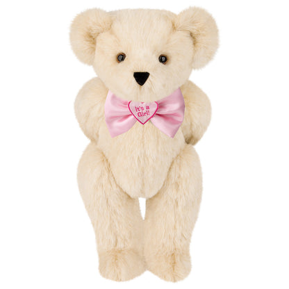 Cream-colored plush teddy bear with a pink satin bow tie embroidered "It's a Girl" and brown eyes.