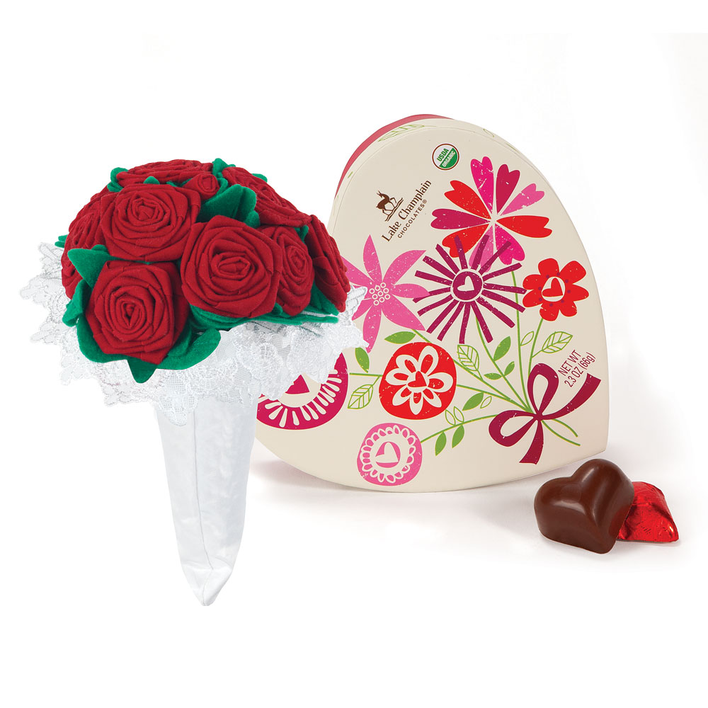 Red velvet rose bouquet wrapped in white lace next to a cream heart-shaped box with colorful floral designs and two.